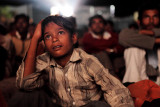 At a Tent Theater Near You.  : A patron of a traveling cinema watches a film at a night screening. Tent cinemas travel to remote villages in India, far from fixed-site theaters. Films are shown in large tents, often using makeshift equipment, with the audience seated on the ground. Although India is home to the most prolific movie industry in the world, producing around 800 films a year, it has one of the lowest ratios of screens to population - 13 screens per million people. The traveling cinemas show mixed fare, including regional language films, Bollywood blockbusters and Hollywood movies, but they are facing a fight for survival as DVDs become more easily accessible and cable networks penetrate further into the country.